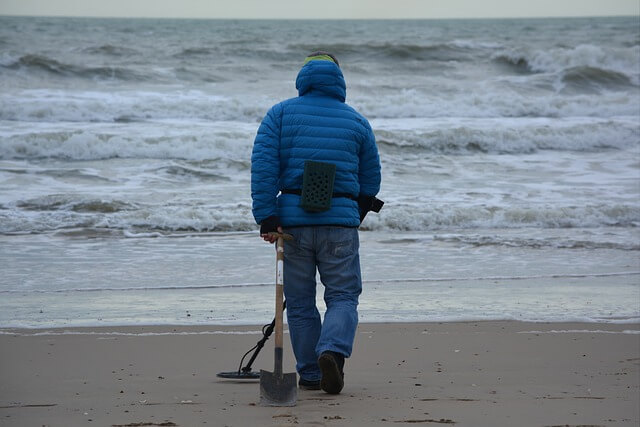 man with blue coat metal detect on beach